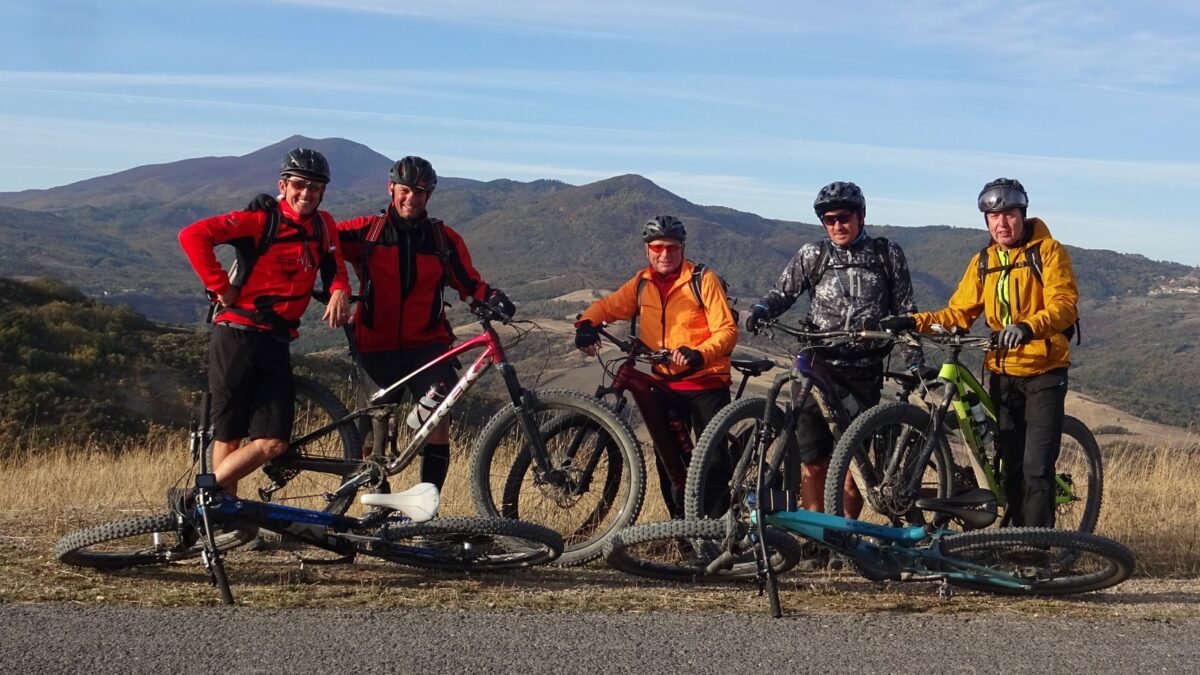 Fünf Mountainbiker stehen vor einer toskanischen Bergkulisse.